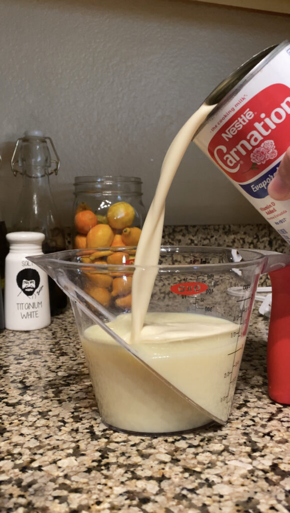 Pouring evaporated milk into sweetened condensed milk in the measuring cup.