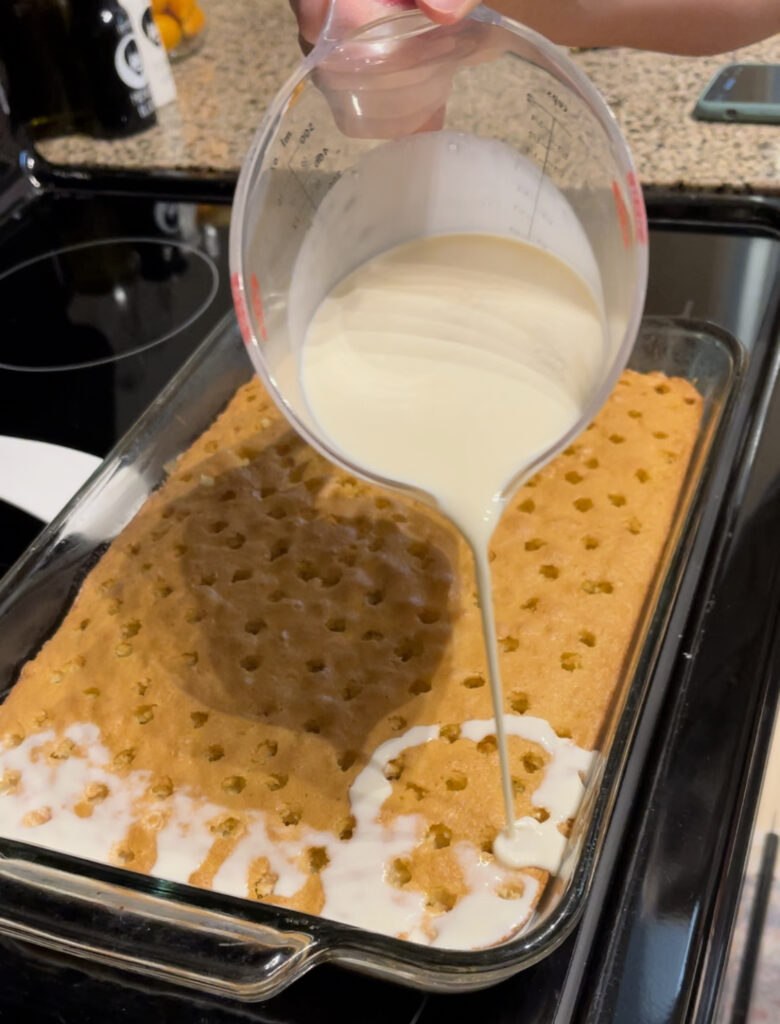 Slowly pouring milk mixture of the cake with holes poked in it.