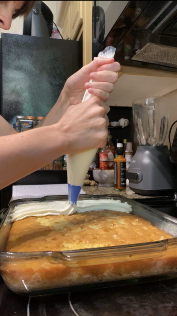 Using a piping bag to spread whip cream on the cake.