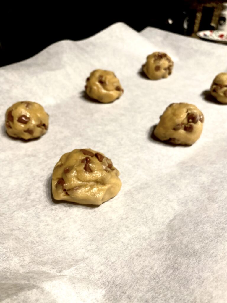 Chocolate chip cookie dough balls on a sheet pan with a piece of parchment underneath