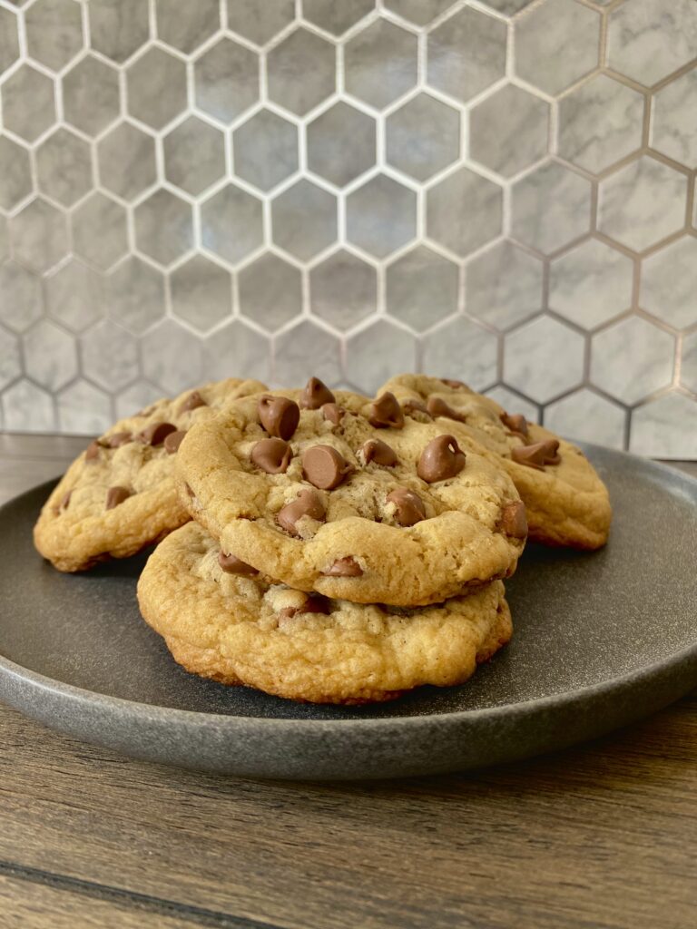 Four chocolate chip cookies stacked on a plate.