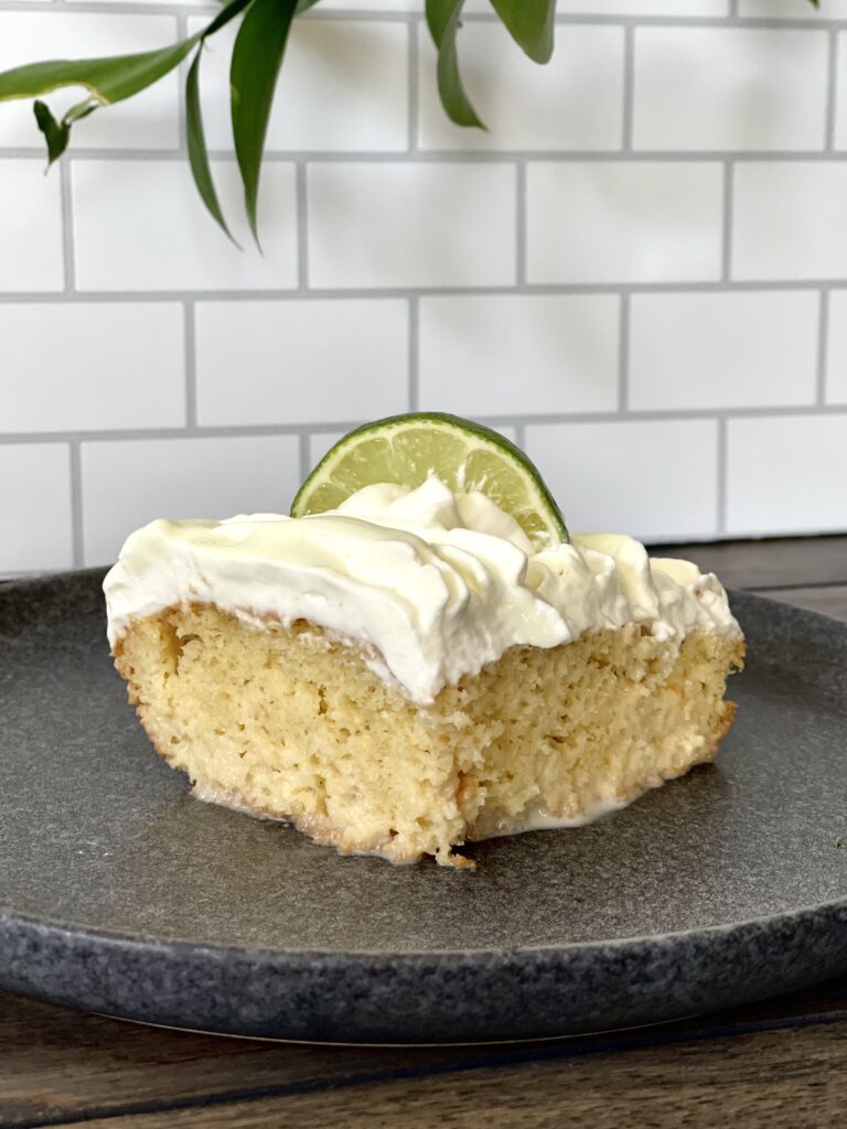 A slice of Tres Leche Cake decorated with whipped cream and a slice of lime.