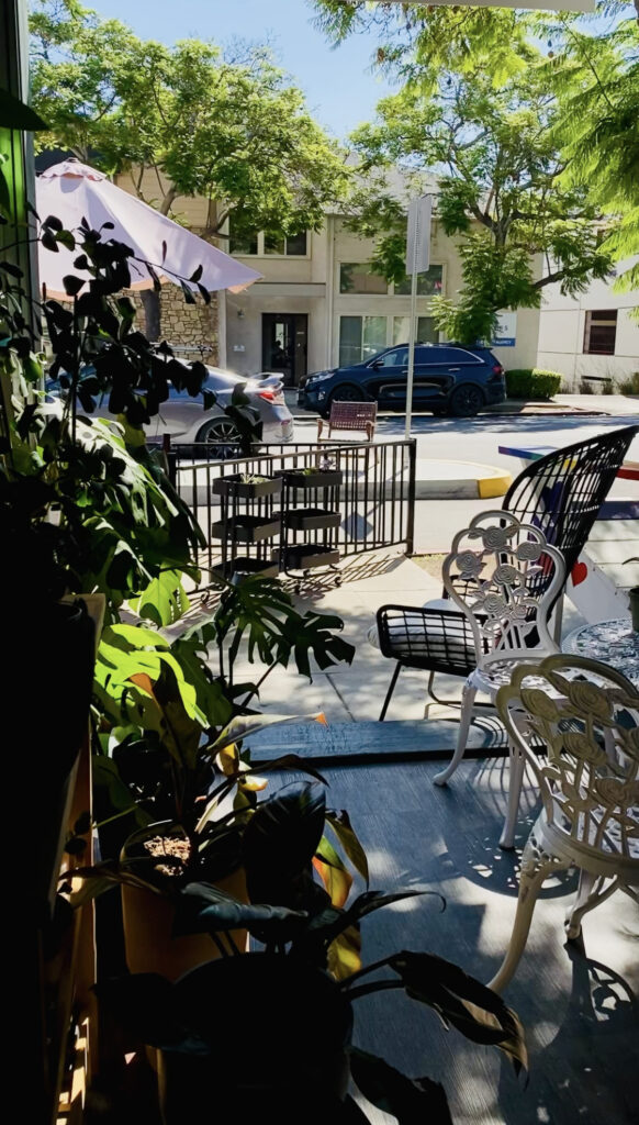 Patio with green plants and decorative white chairs.