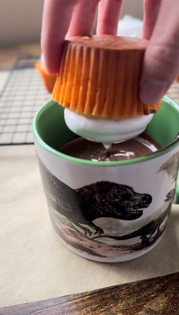 Dipping a hi-hat frosted cupcake in melted chocolate.