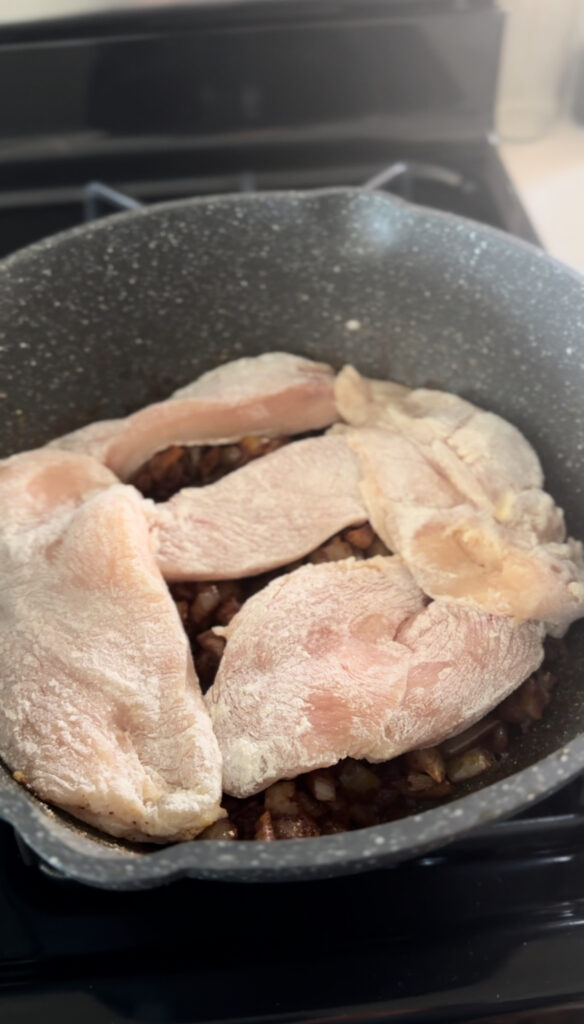 Chicken coated in flour in frying pan with onion mixture for chicken paprikash