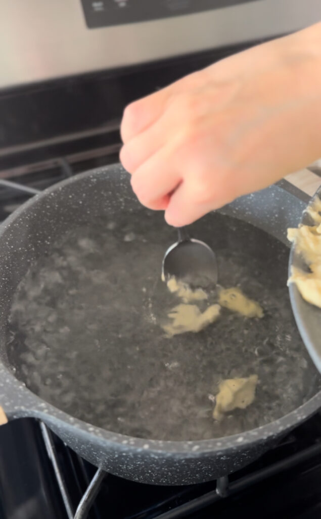 scraping small blobs of dumpling into boiling water