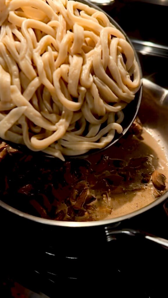 Adding noodles to sauce for creamy mushroom noodle sauce