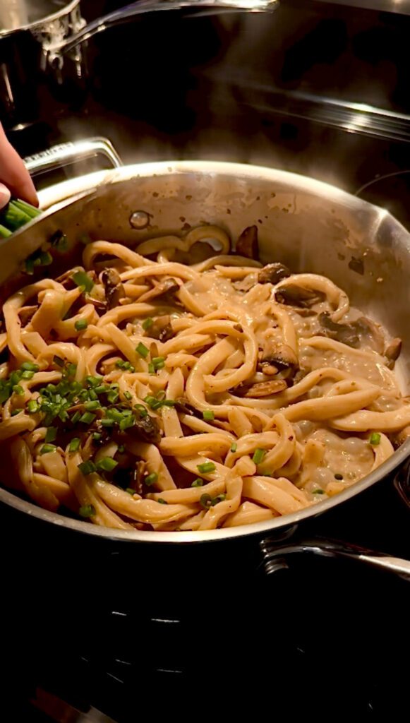Adding toppings to creamy mushroom udon noodles