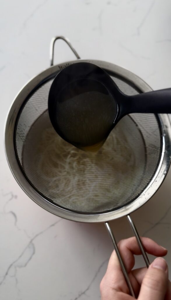 Pouring chicken broth over noodles through a sieve