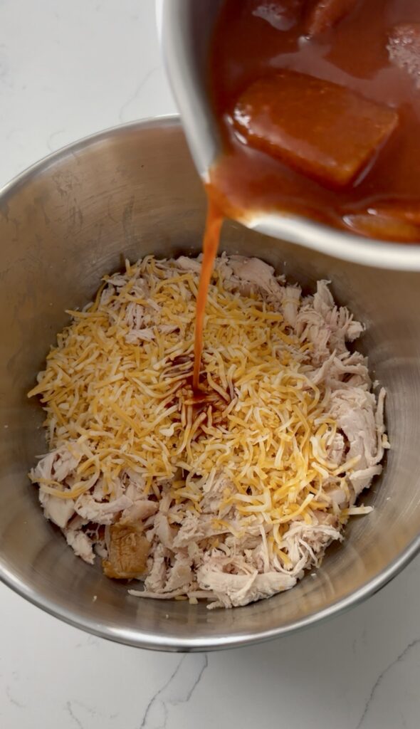 pouring enchilada sauce in chicken and cheese mixture