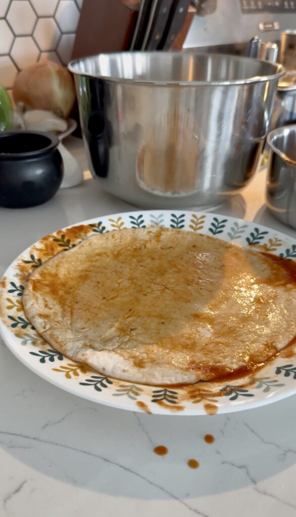 flipping tortilla in red sauce for enchiladas