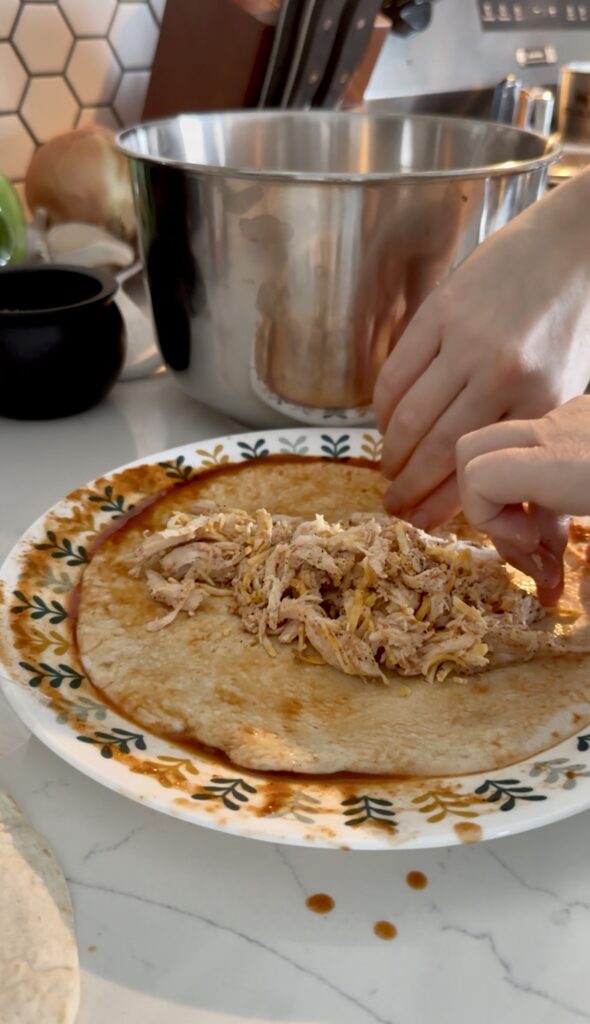 Rolling up an enchilada full of a shredded chicken mixture.