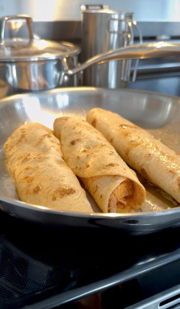 Three rolled chicken enchiladas in a frying pan