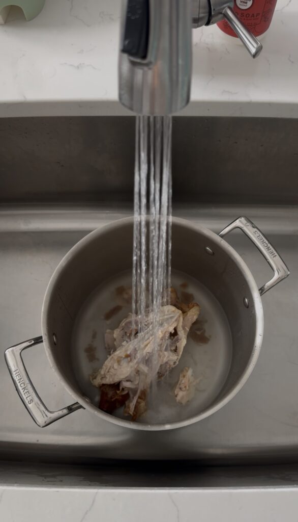 chicken bones in a stock pot with water being added to it to cover the chicken