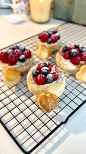 Four flaky pastries topped with custard, raspberries, blueberries and spinkle of powdered sugar.