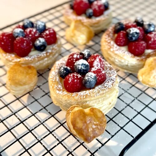 Four flaky pastries topped with custard, raspberries, blueberries and spinkle of powdered sugar.