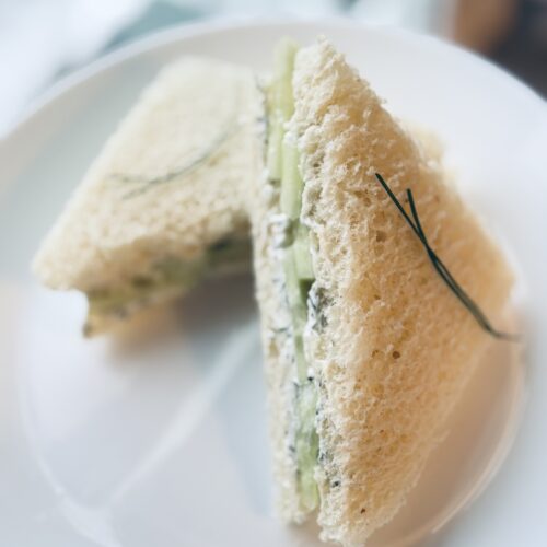 cucumber tea sandwiches served on a plate neatly with a cup of tea