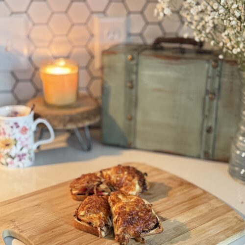 cheese toasties sliced and stacked on a cutting board with a candle lit and flowers in the back