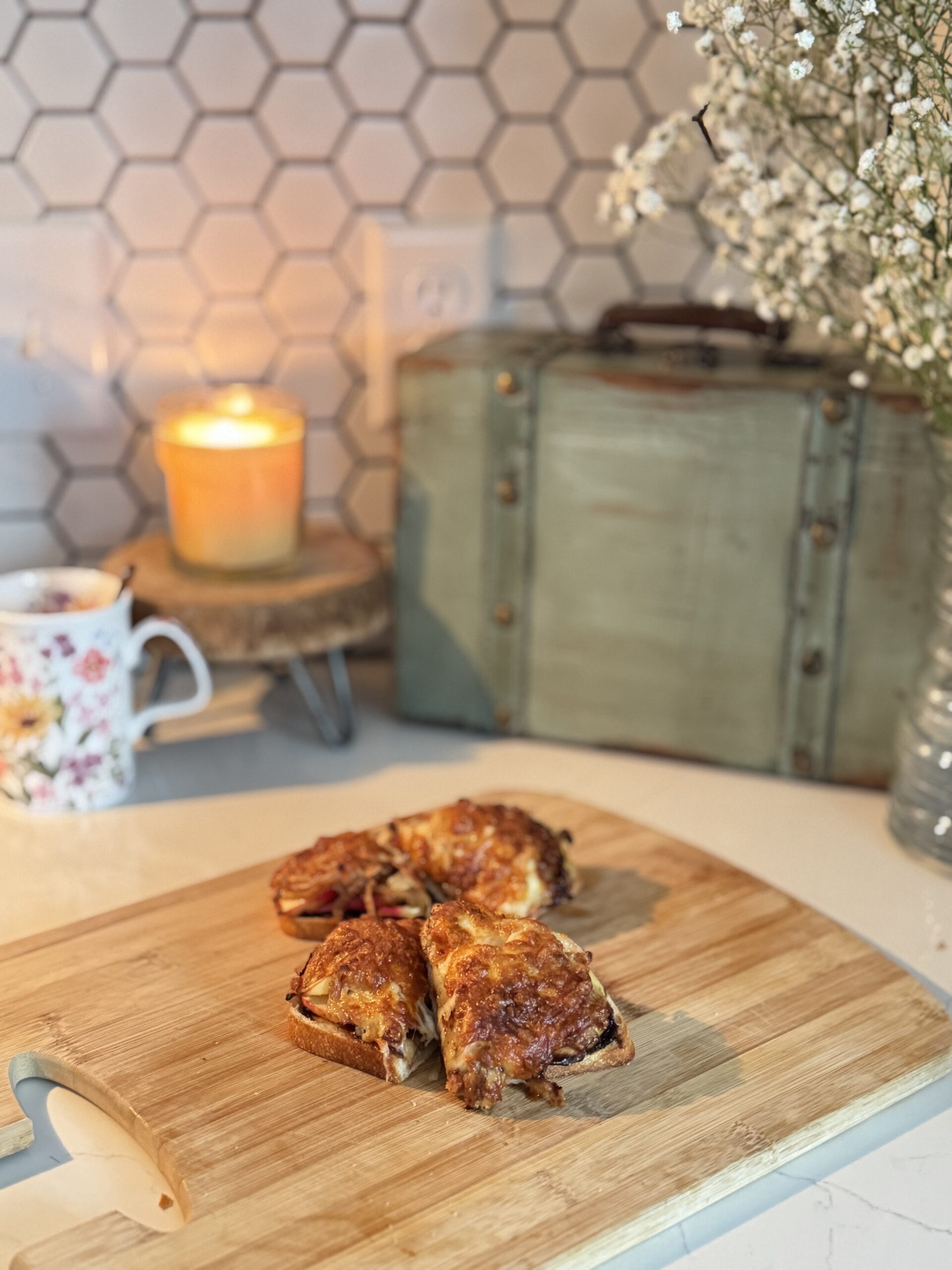 cheese toasties sliced and stacked on a cutting board with a candle lit and flowers in the back
