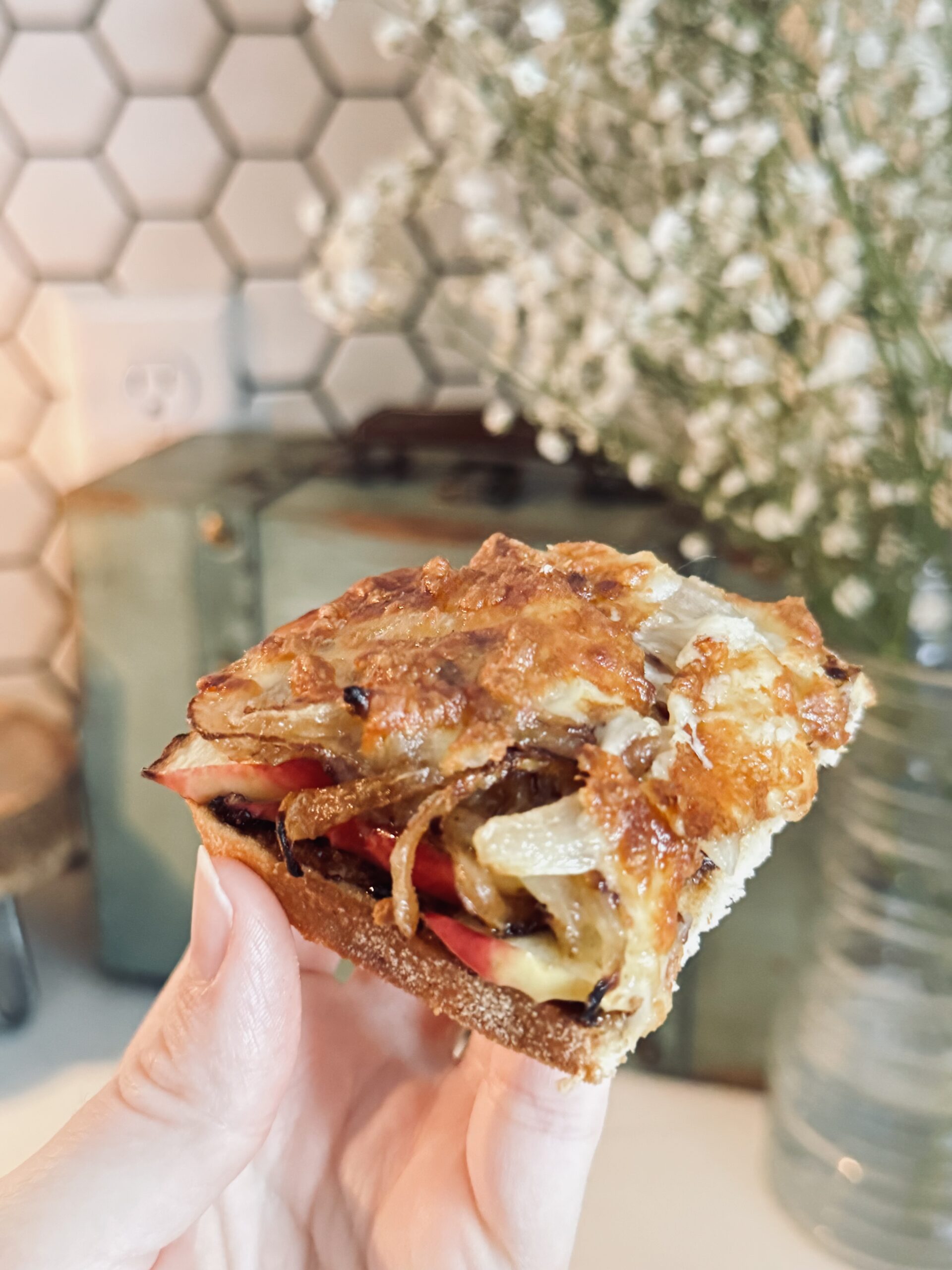 holding the cheese toasty in a hand and flowers behind it.