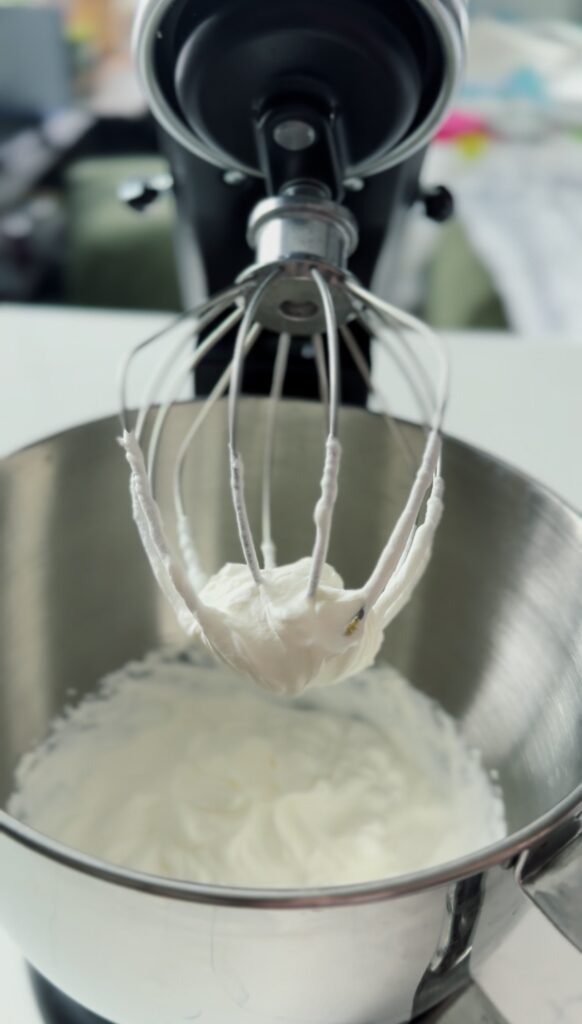 a whisk covered in whipped cream in a stand mixer