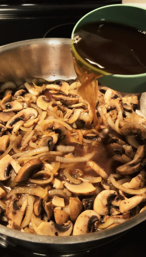 Adding beef broth to the mushrooms and onions