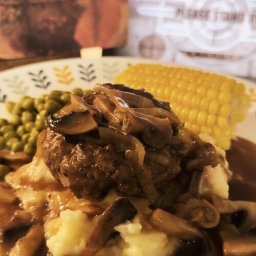 Salisbury steak smothered in mushroom gravy sauce over mashed potatoes. With corn and peas on the side. A saddle up salisbury tv dinner box in the background.