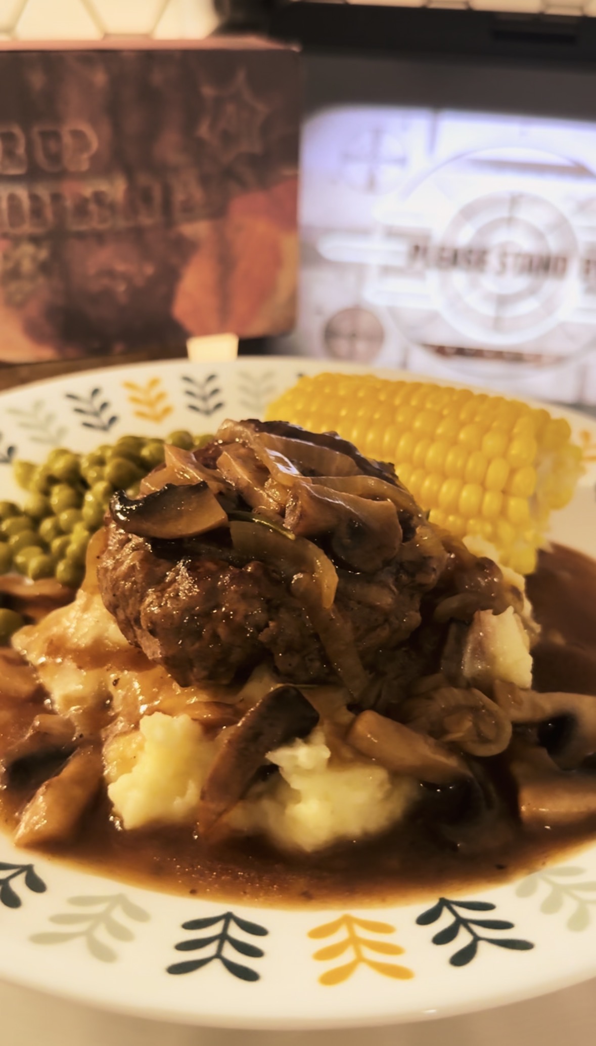 Salisbury steak smothered in mushroom gravy sauce over mashed potatoes. With corn and peas on the side. A saddle up salisbury tv dinner box in the background.