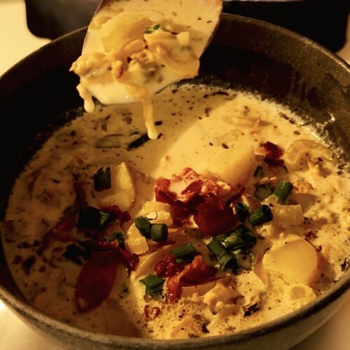 A spoon full of clam chowder hovering over a bowl full of soup