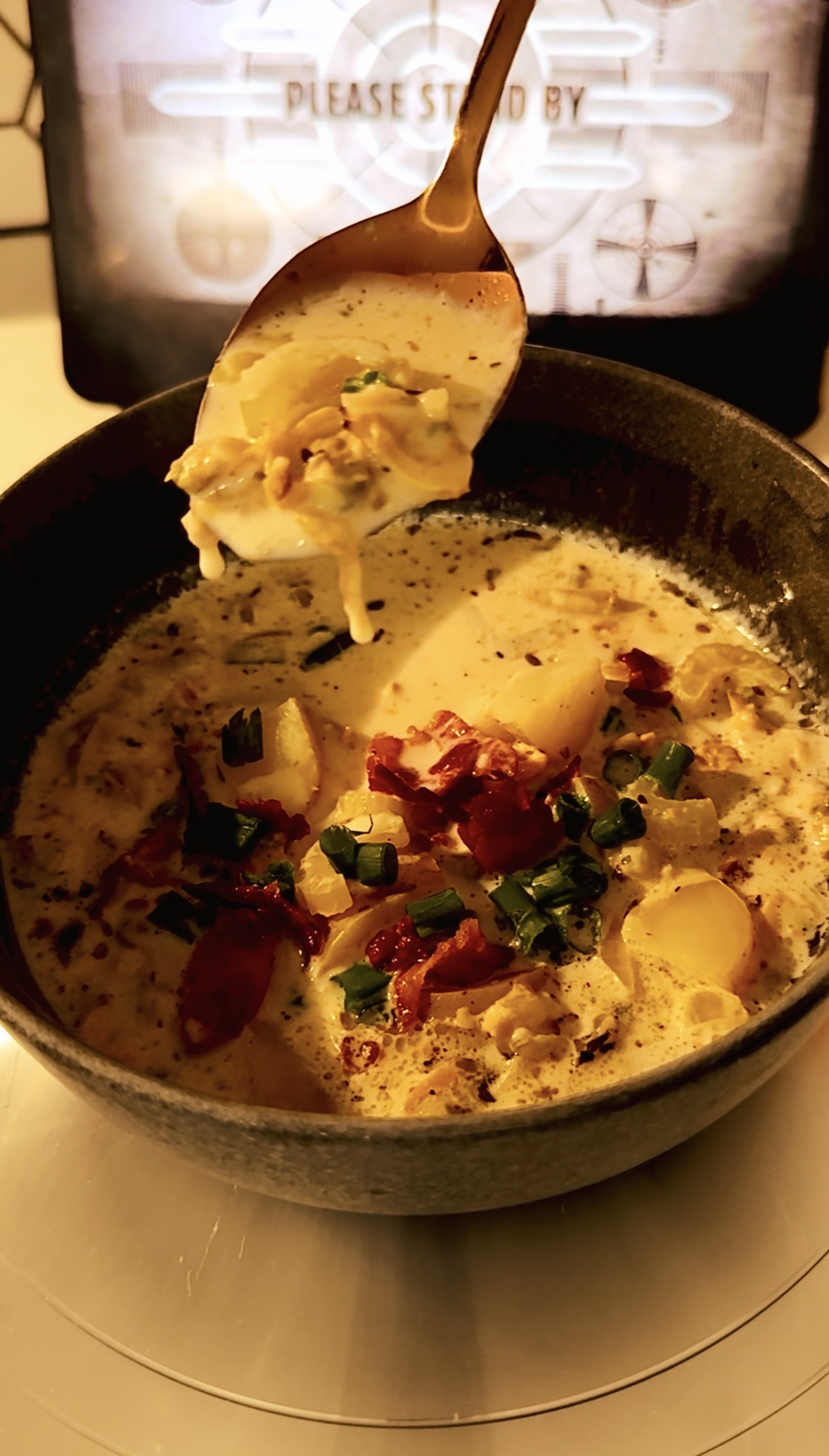 A spoon full of clam chowder hovering over a bowl full of soup