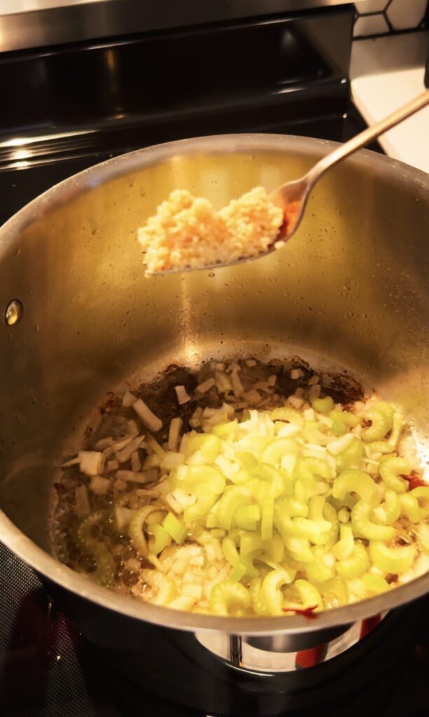 A fork full of garlic going into the stock pot with celery and onion